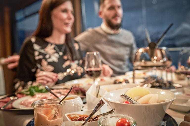 Sauces and side dishes on laid table for Fondue Chinoise, a man and a woman sitting on the table